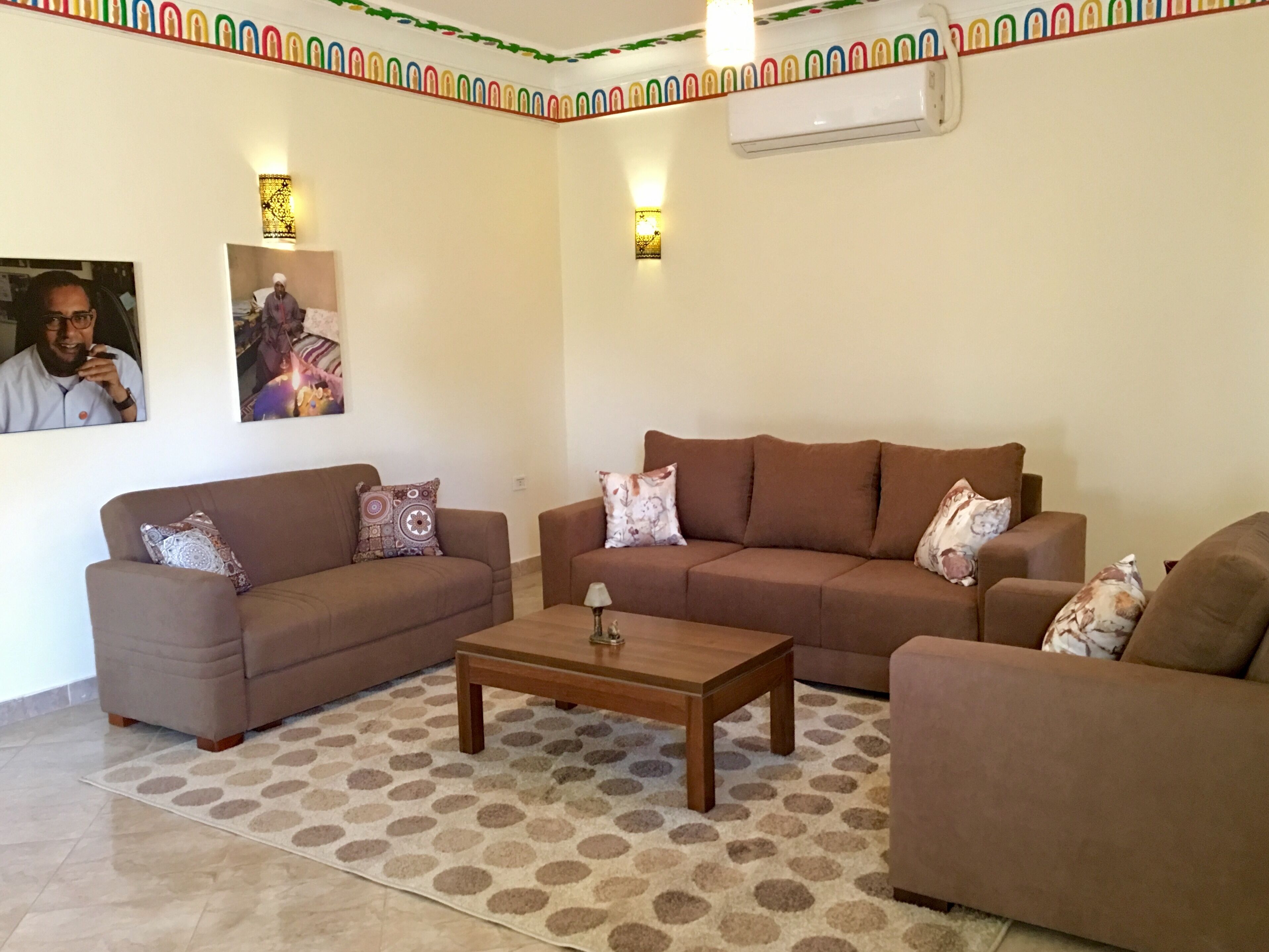 Una sala de estar con dos sofás, una mesa de centro, alfombra estampada, luces fijadas a la pared y un cuadro enmarcado.