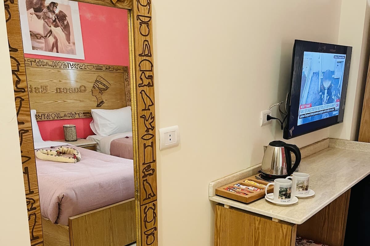 Hotellihuone, jossa on puinen sänky, pieni työpöytä, jossa on televisio, vedenkeitin ja kuppi.