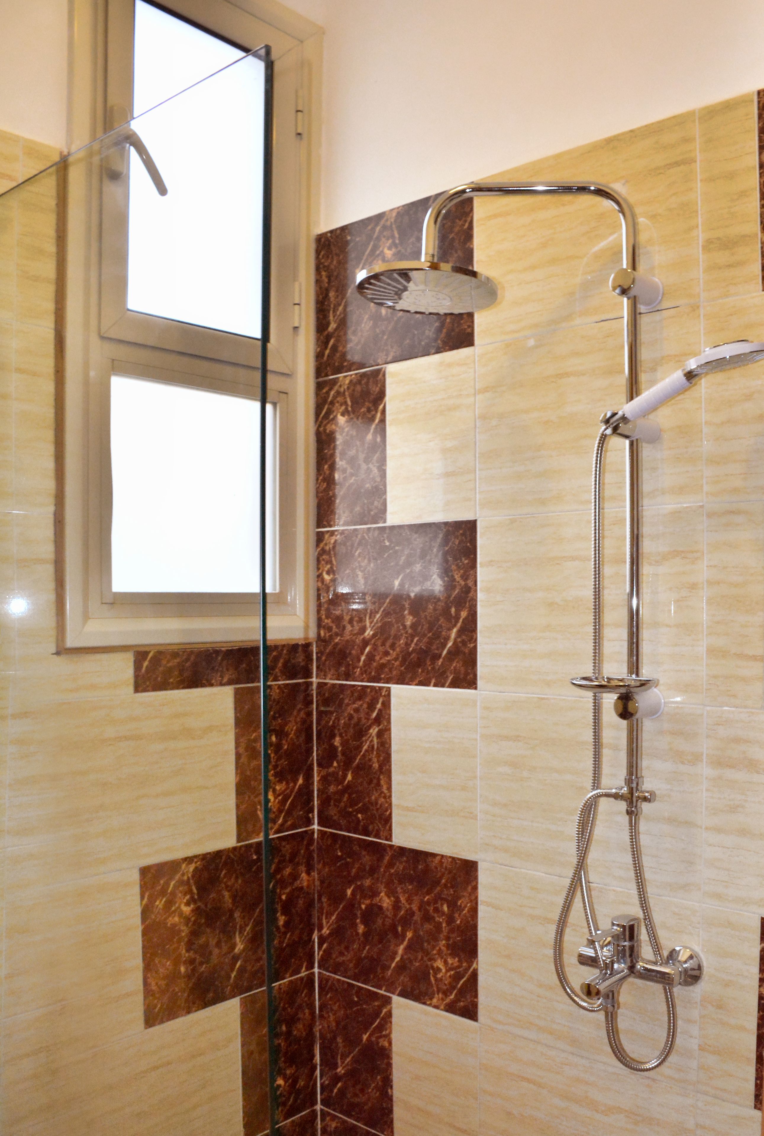 A shower with a handheld showerhead and a wall-mounted faucet, set against a backdrop of marble tiles with a geometric pattern.