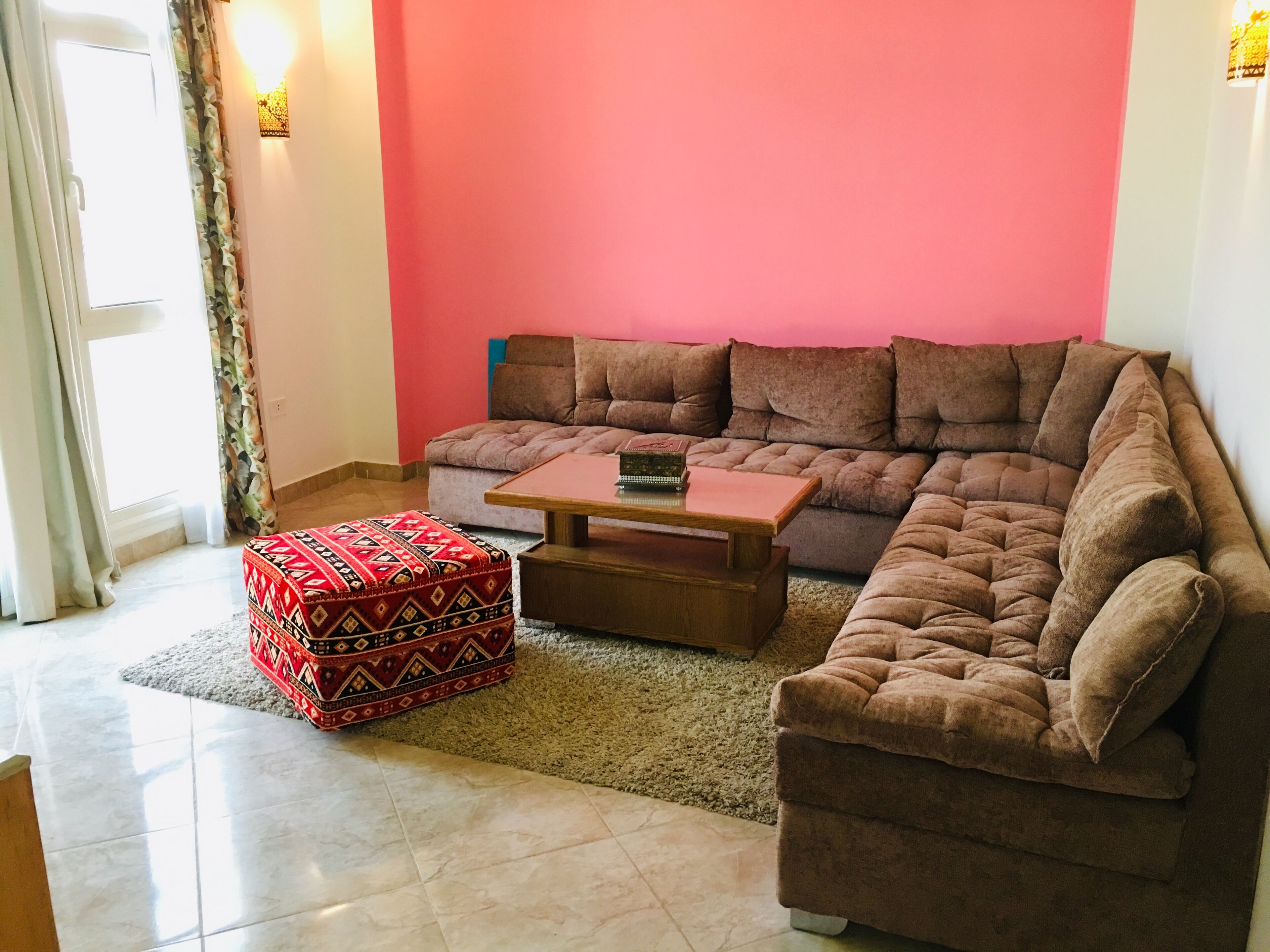 A living room with a sectional sofa, a coffee table, and a patterned ottoman.