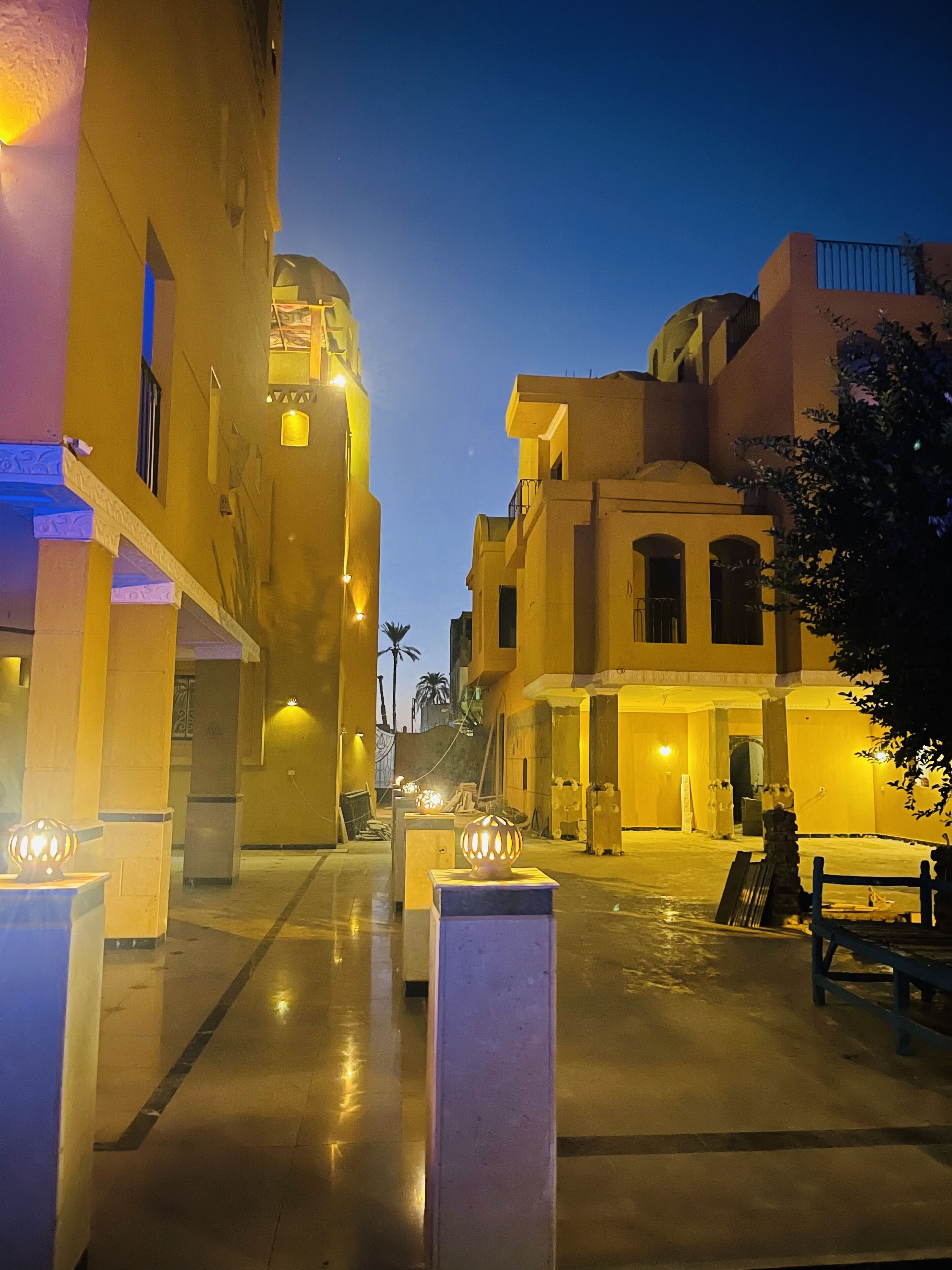 Vista nocturna de una calle estrecha flanqueada por edificios, con ventanas y puertas iluminadas y un sendero pavimentado.