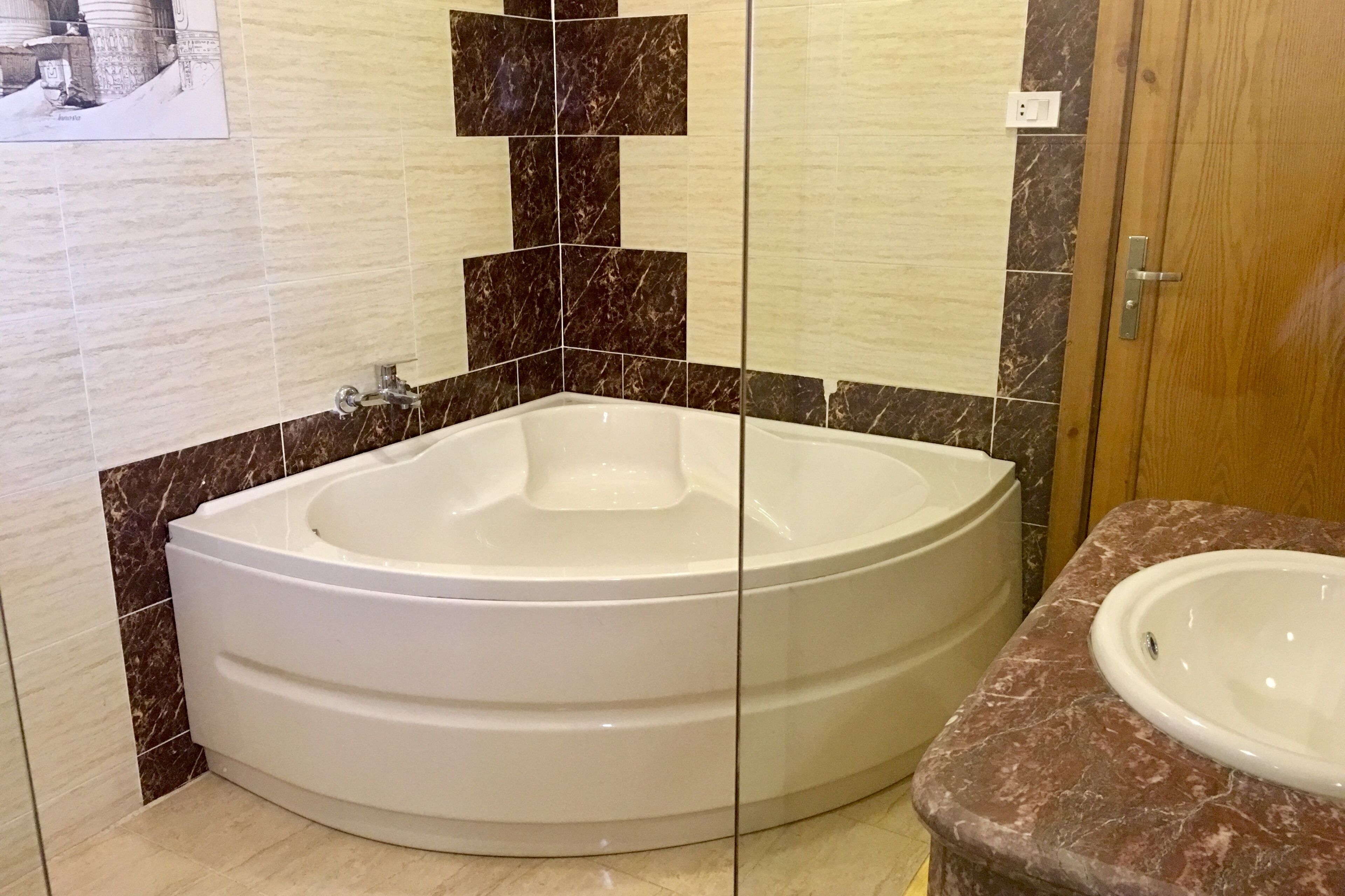 A bathroom with a large bathtub, a sink, and marble tiles.