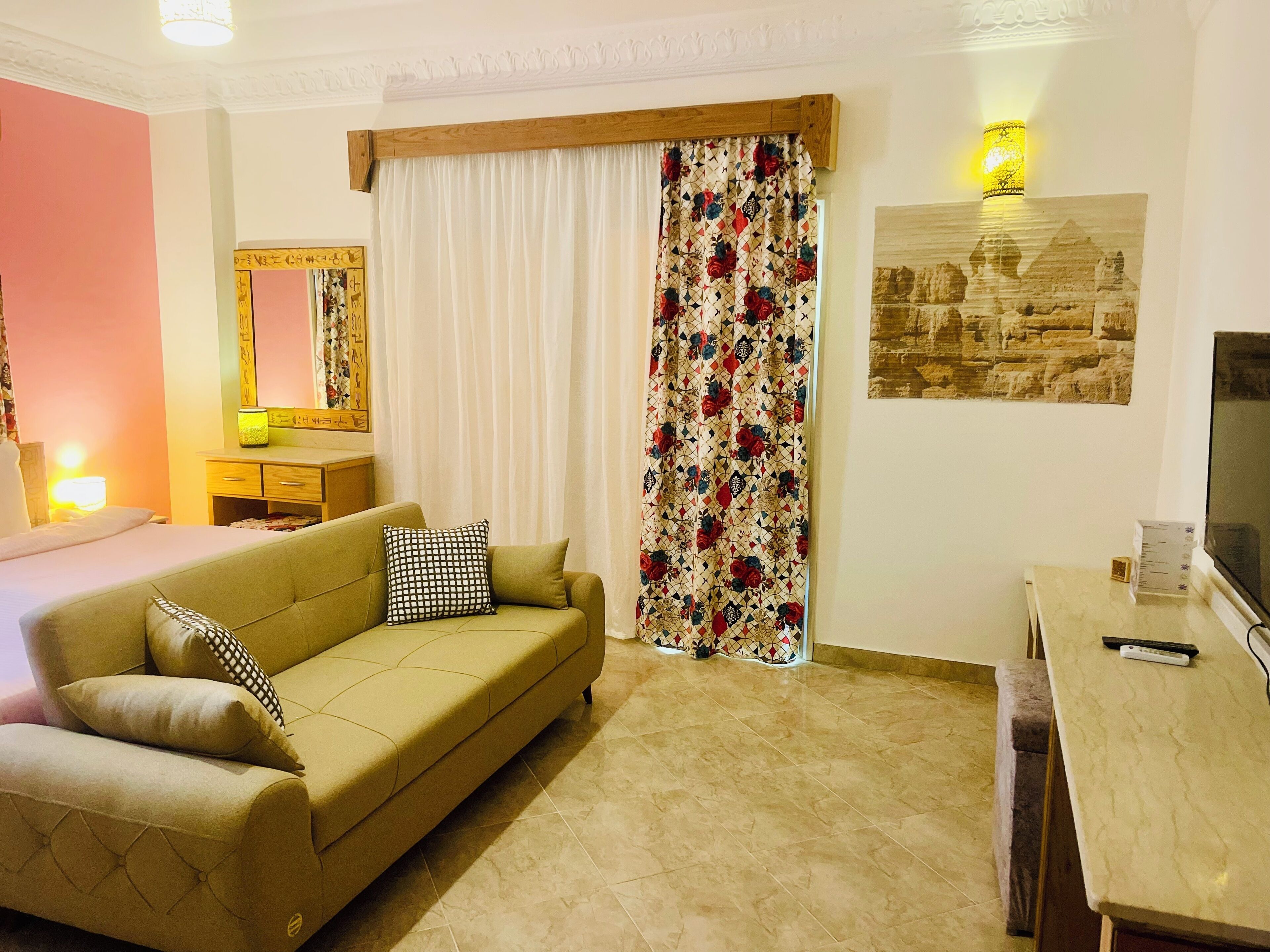 Ein Hotelzimmer mit Bett, Sofa, Schreibtisch, Fernseher, Spiegel und Vorhang mit Blumenmuster.