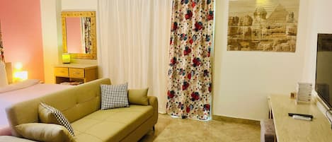 A hotel room with a bed, a sofa, a desk, a TV, a mirror, and a curtain with a floral pattern.