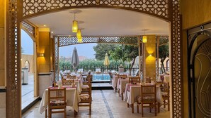 An indoor dining area with tables and chairs, a pool view, and decorative wooden lattice. - Jewel Howard Carter Hotel (Luxor)
