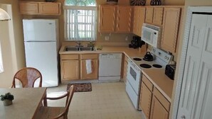 A compact kitchen with wooden cabinets, a white refrigerator, a microwave, and a stove. - Ly53817 - Indian Ridge - 3 Bed 2 Baths Villa (Kissimmee)