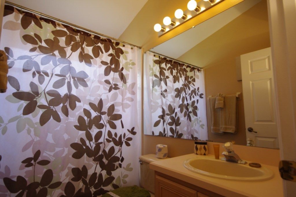 A bathroom with a mirror, sink, and shower curtain with a leaf pattern.