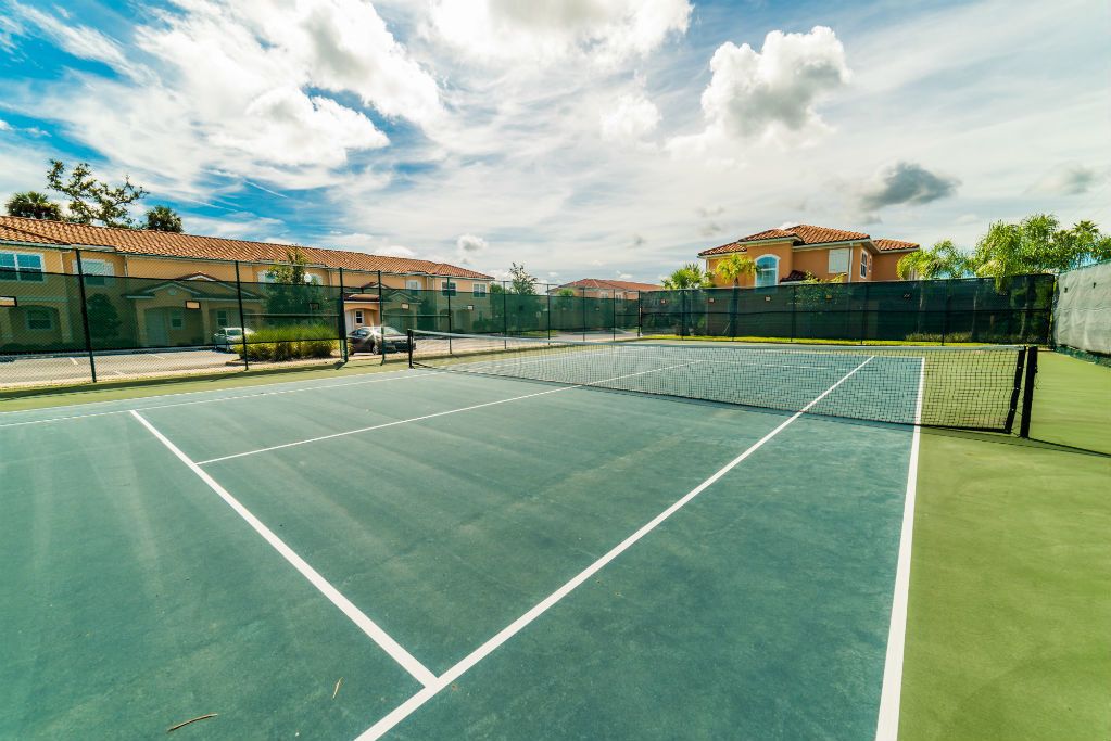 A tennis court with a net, surrounded by a fence and buildings.