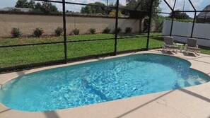 A rectangular swimming pool with clear blue water, surrounded by a concrete deck and a black fence.