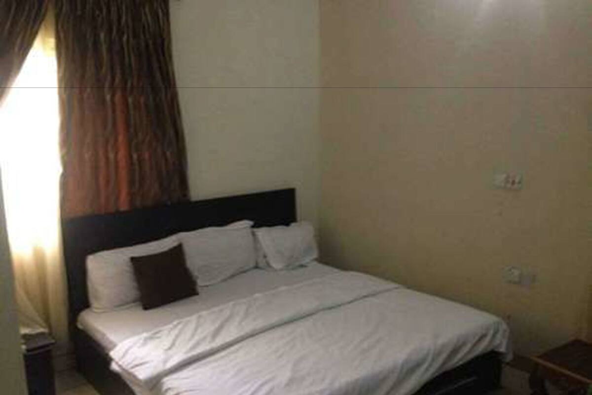 A small, single-bed room with a plain headboard, a bedside table, and a curtain.