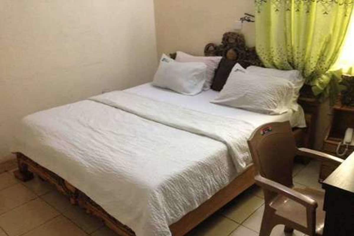 A single bed with a wooden frame, a white bedspread, and a nightstand with a lamp.