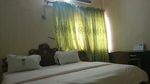 A single bed with a wooden headboard, a desk with a chair, and a window with green curtains. - Ekulu Greens Classic Suites (Enugu)