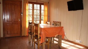 Un comedor con una mesa y sillas de madera, un ventanal con cortinas y un televisor montado en la pared.