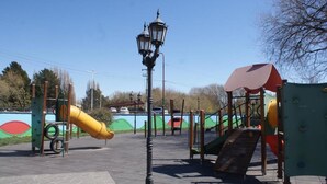 Un parque infantil con toboganes y estructuras para escalar, una farola y un cielo despejado.