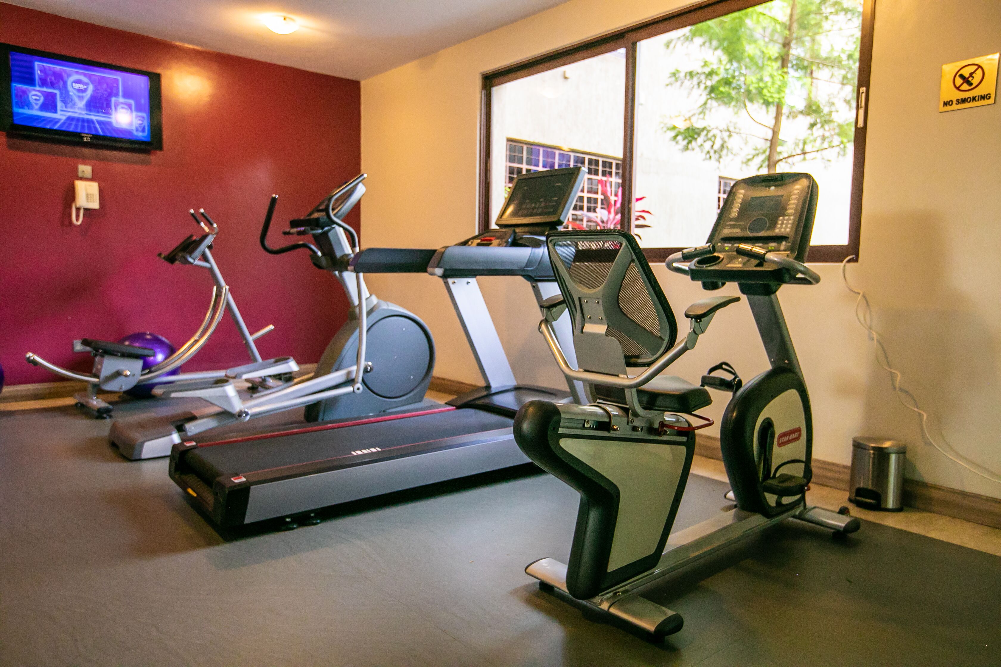 Une salle de sport équipée de tapis de course, de vélos elliptiques et d’un écran de télévision diffusant un événement sportif.