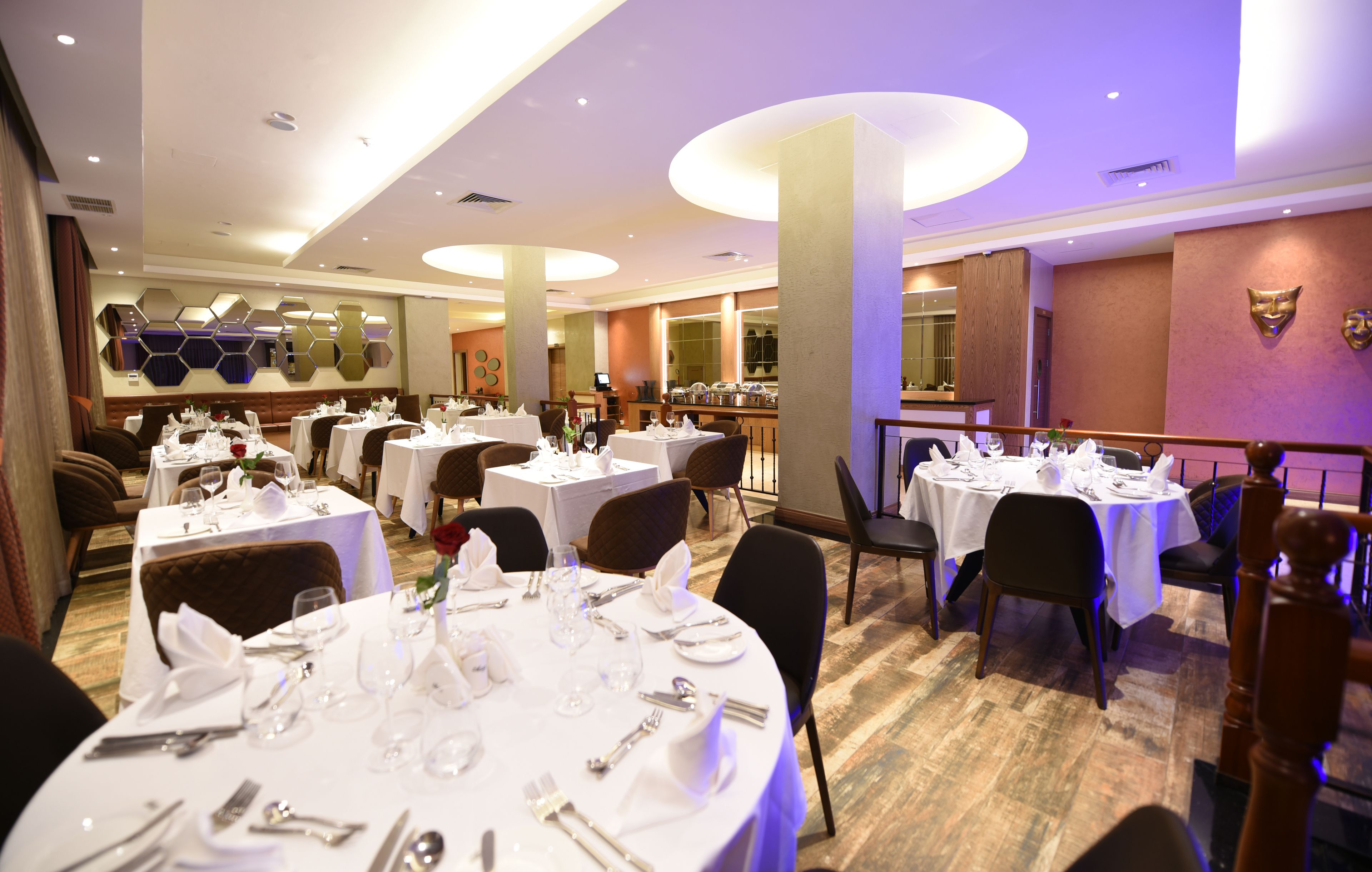 Une salle à manger d’hôtel avec des tables rondes dressées pour le repas, agrémentée de nappes blanches, de couverts soigneusement disposés et de verres élégants.