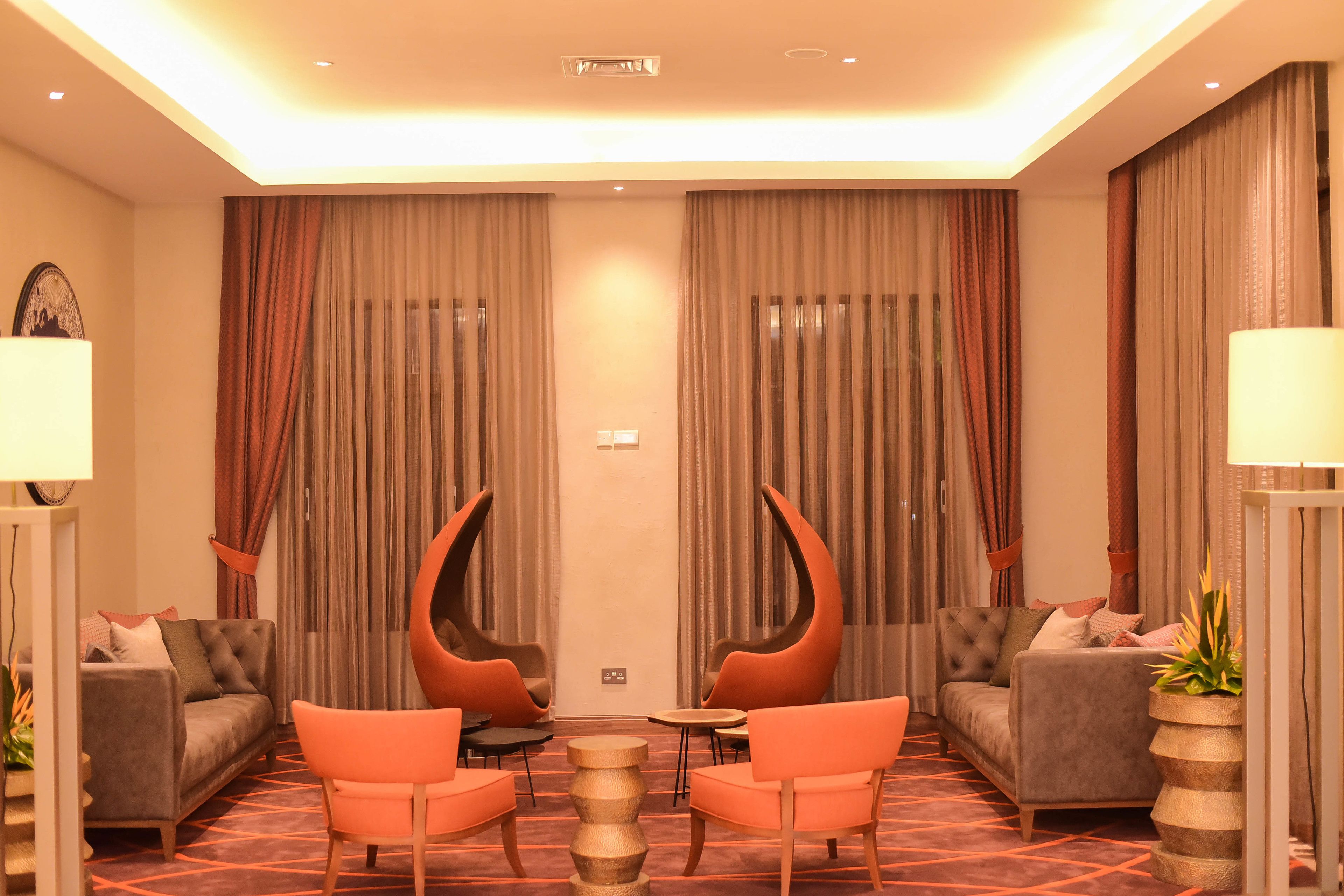 Quarto de hotel moderno com um sofá, duas poltronas, uma mesa de centro e um vaso de planta.
