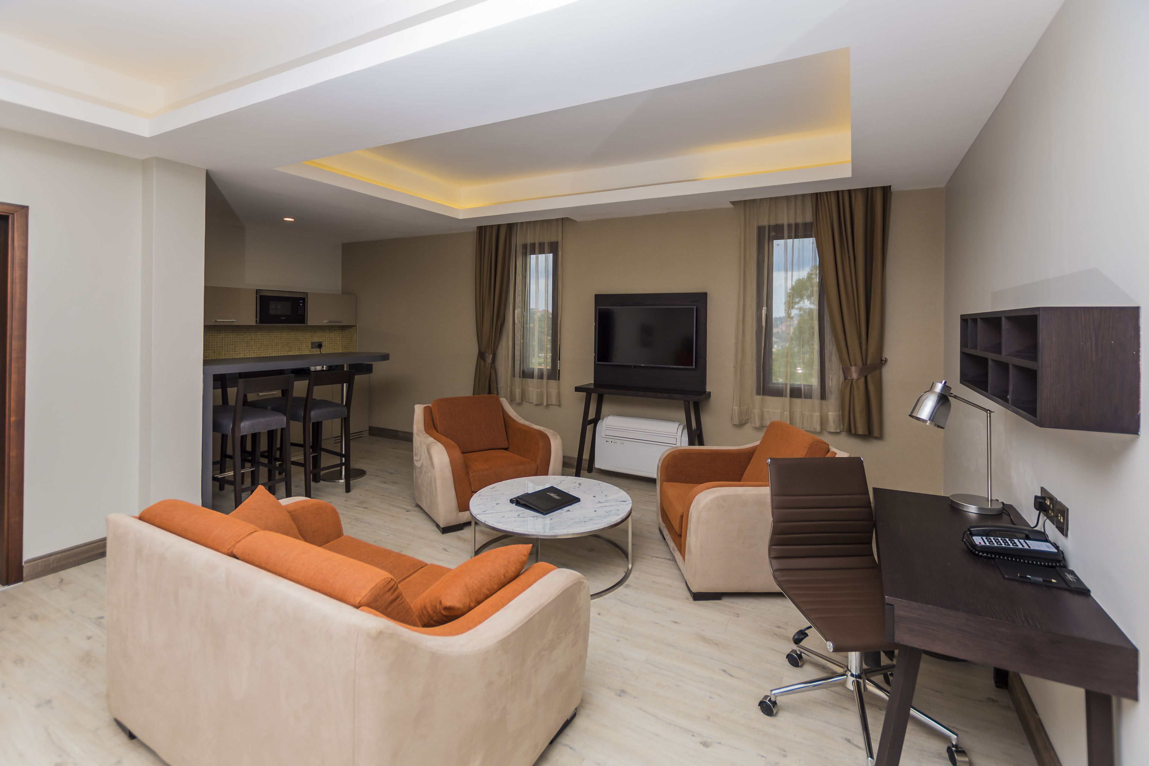 Una sala de estar moderna con sofá, sillones, una mesa de centro, un escritorio con ordenador y televisión.