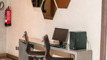 Um espaço de escritório moderno com um painel de espelhos hexagonais, duas cadeiras de escritório, uma escrivaninha com um computador e um extintor de incêndio na parede.