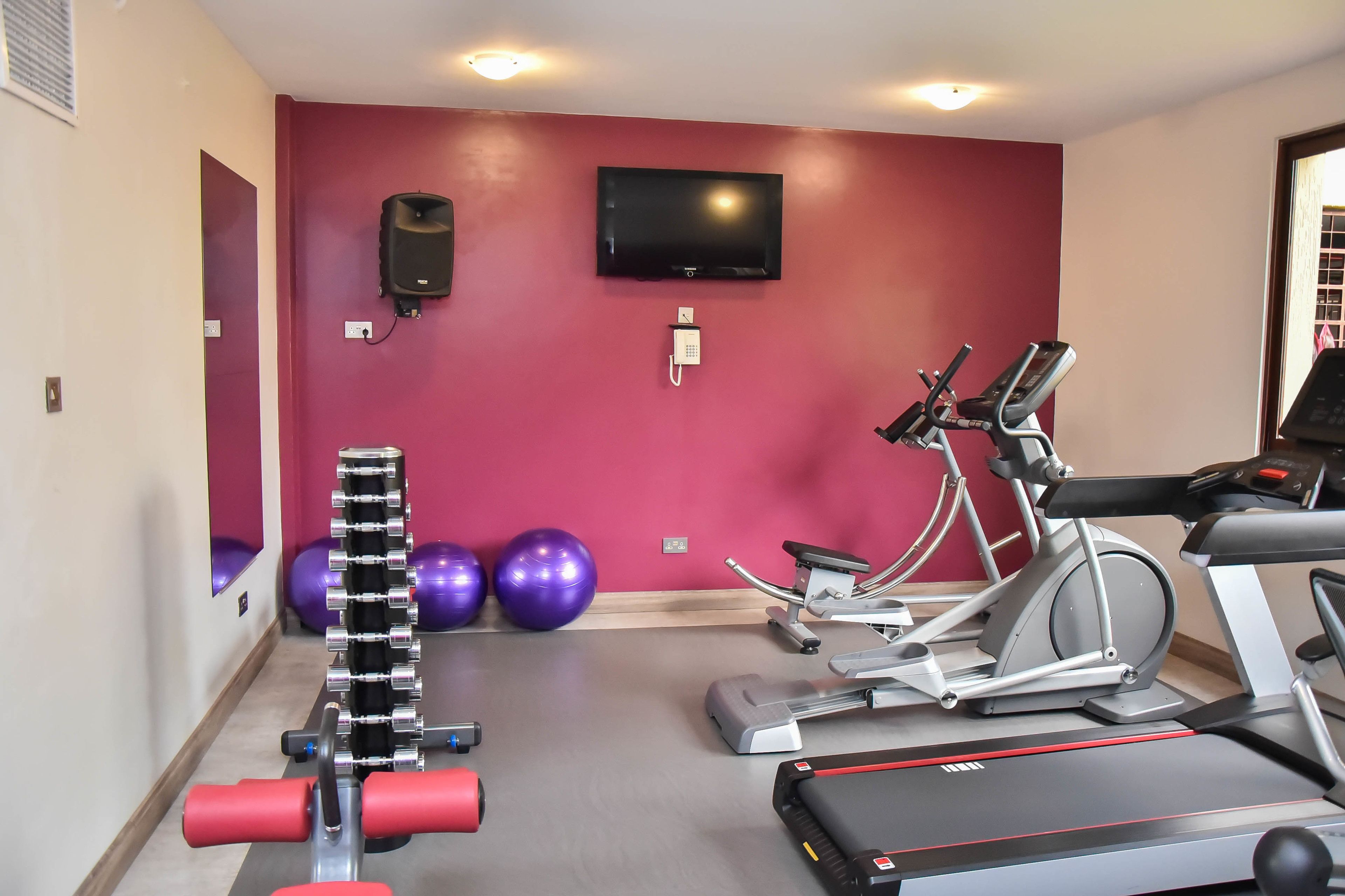 Une salle de sport équipée de matériel d’exercice, avec un téléviseur et un téléphone fixé au mur.