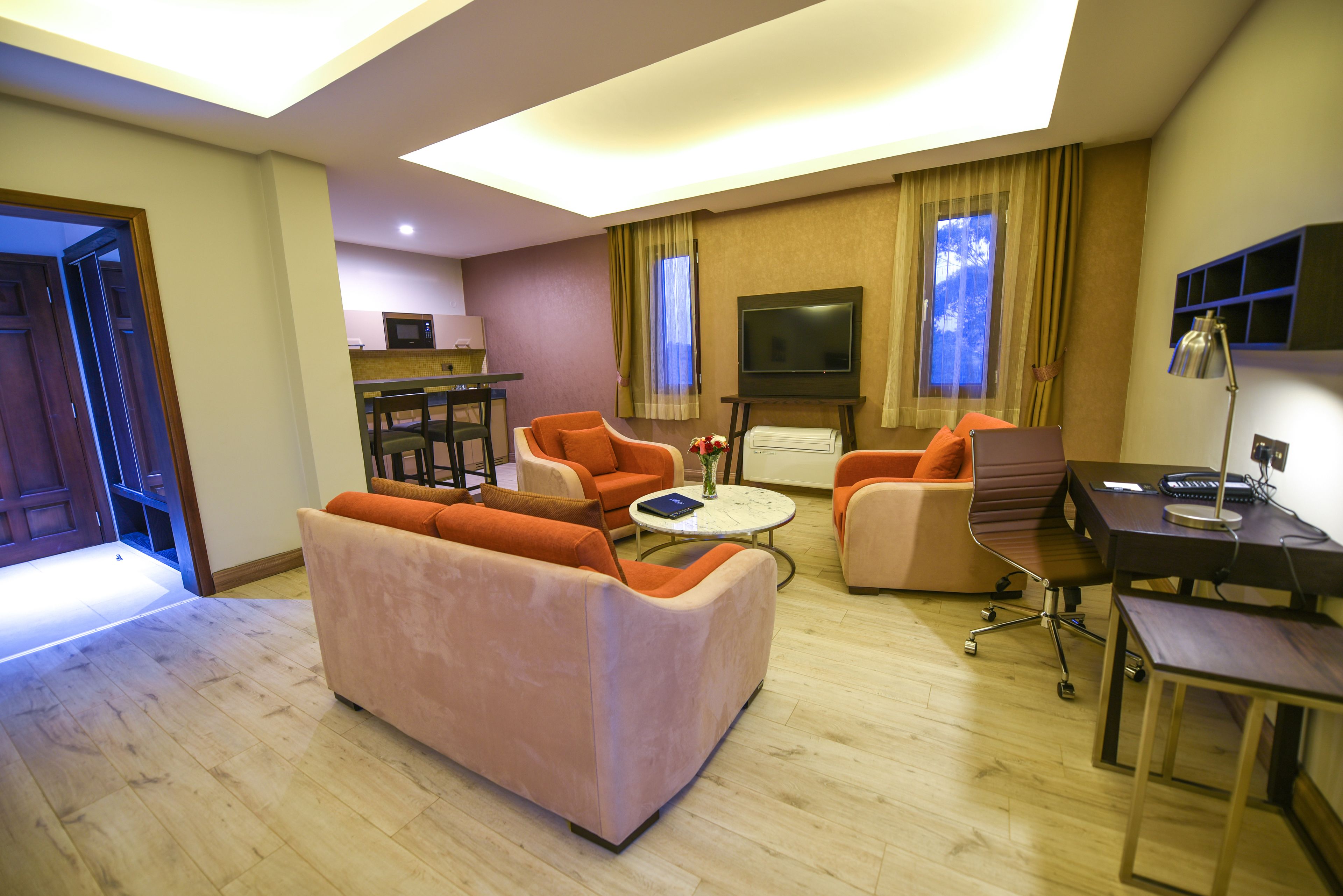 Una sala de estar moderna con sofá, sillones, una mesa de centro, televisor y un escritorio con lámpara.