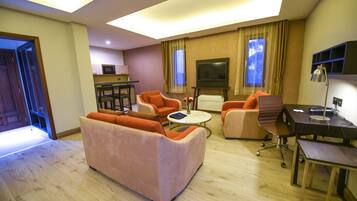 Un salon moderne comprenant un canapé, des fauteuils, une table basse, un téléviseur et un bureau avec une lampe.