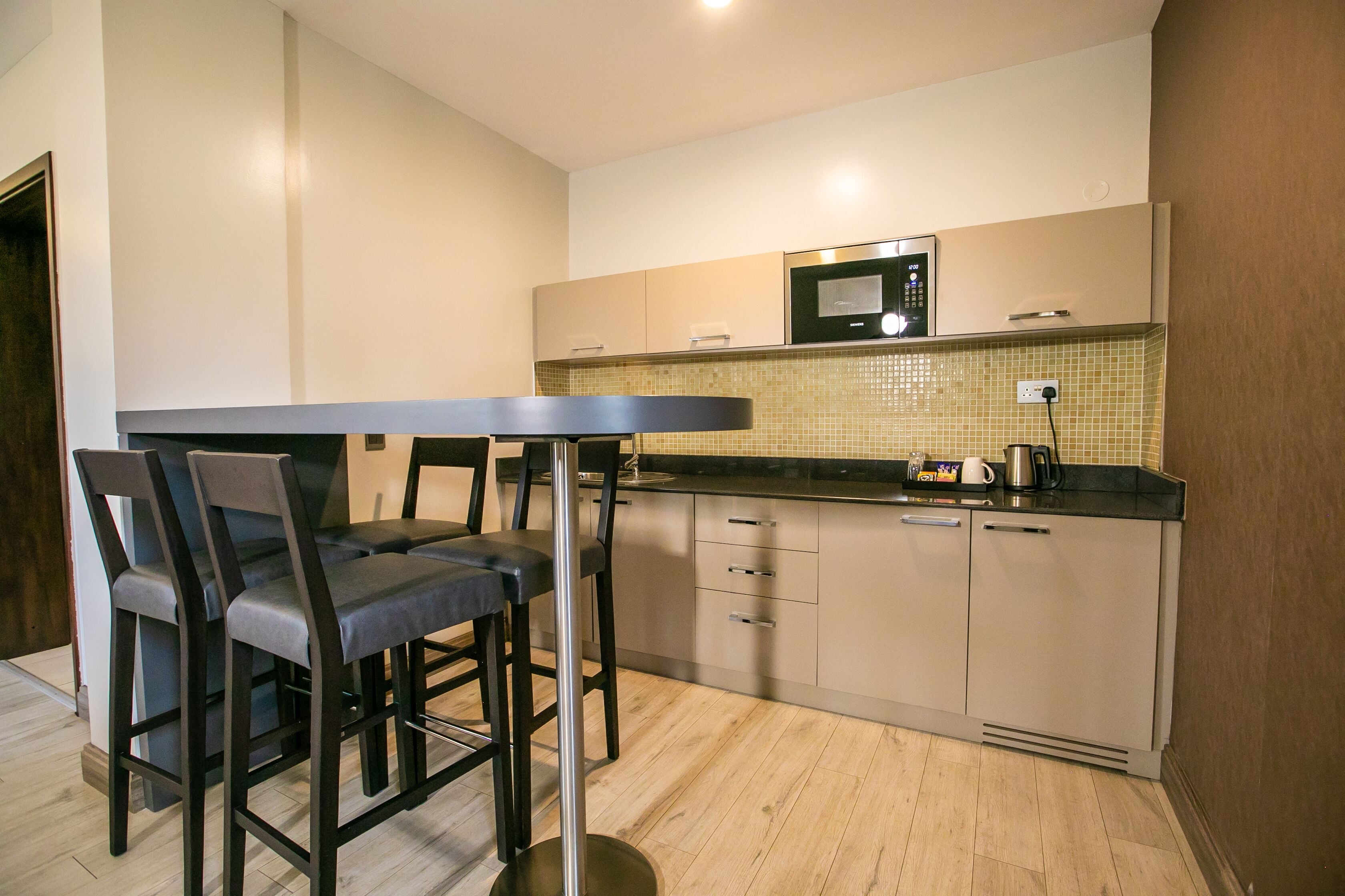 A modern kitchen with a dining area, featuring a black table and chairs, a microwave, and a tiled backsplash.