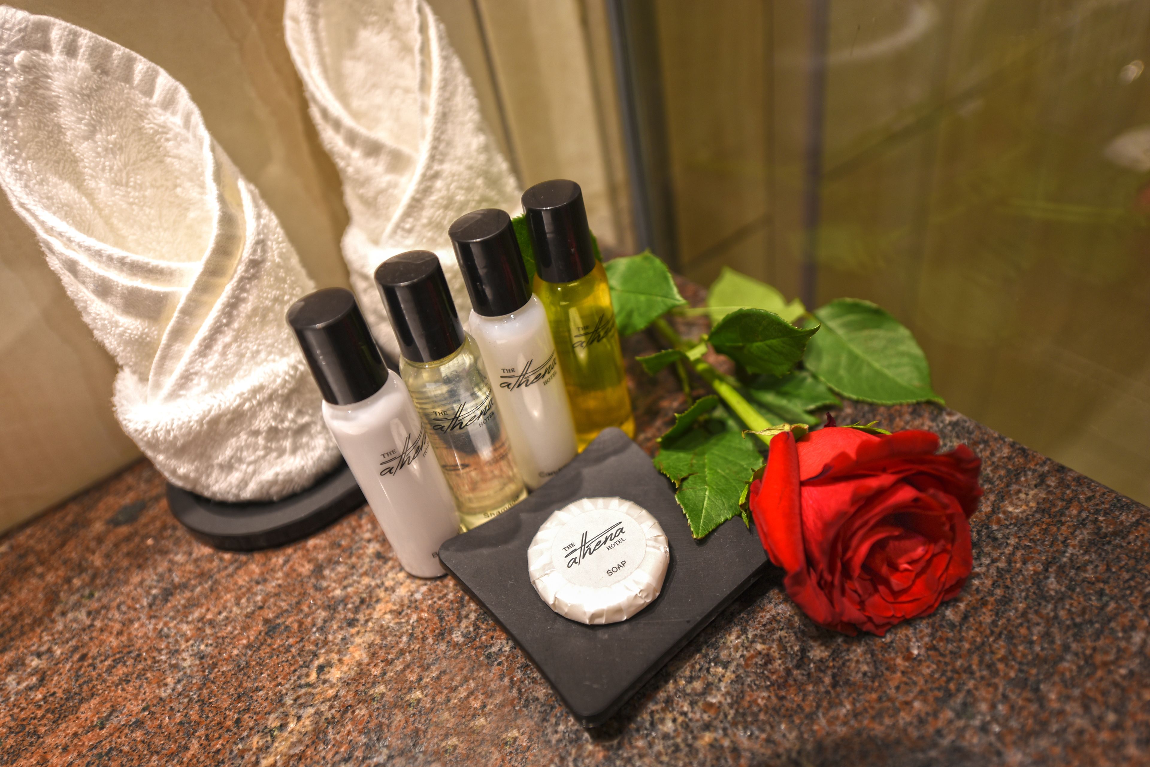 Una encimera de baño con artículos de aseo, una pastilla de jabón y una rosa roja.