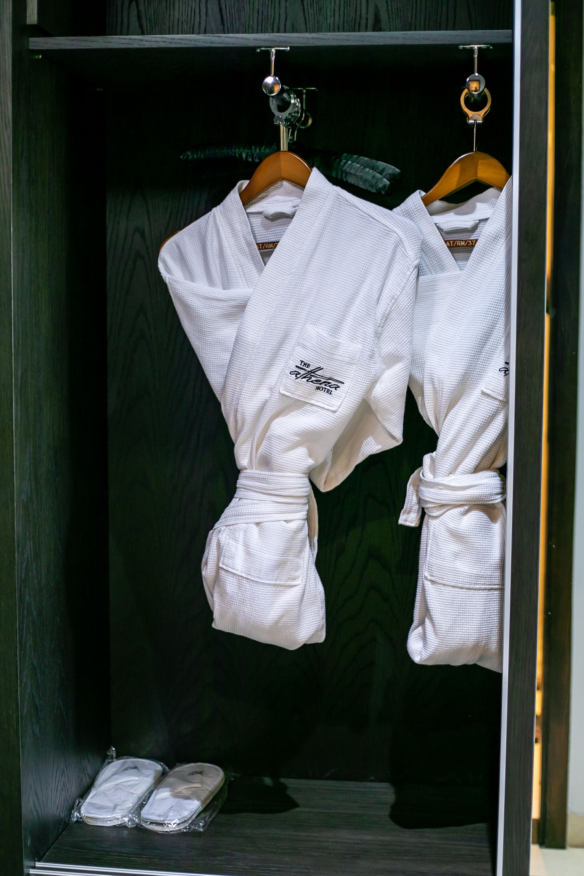 Um guarda-roupa de madeira com dois roupões brancos pendurados em cabides de madeira.