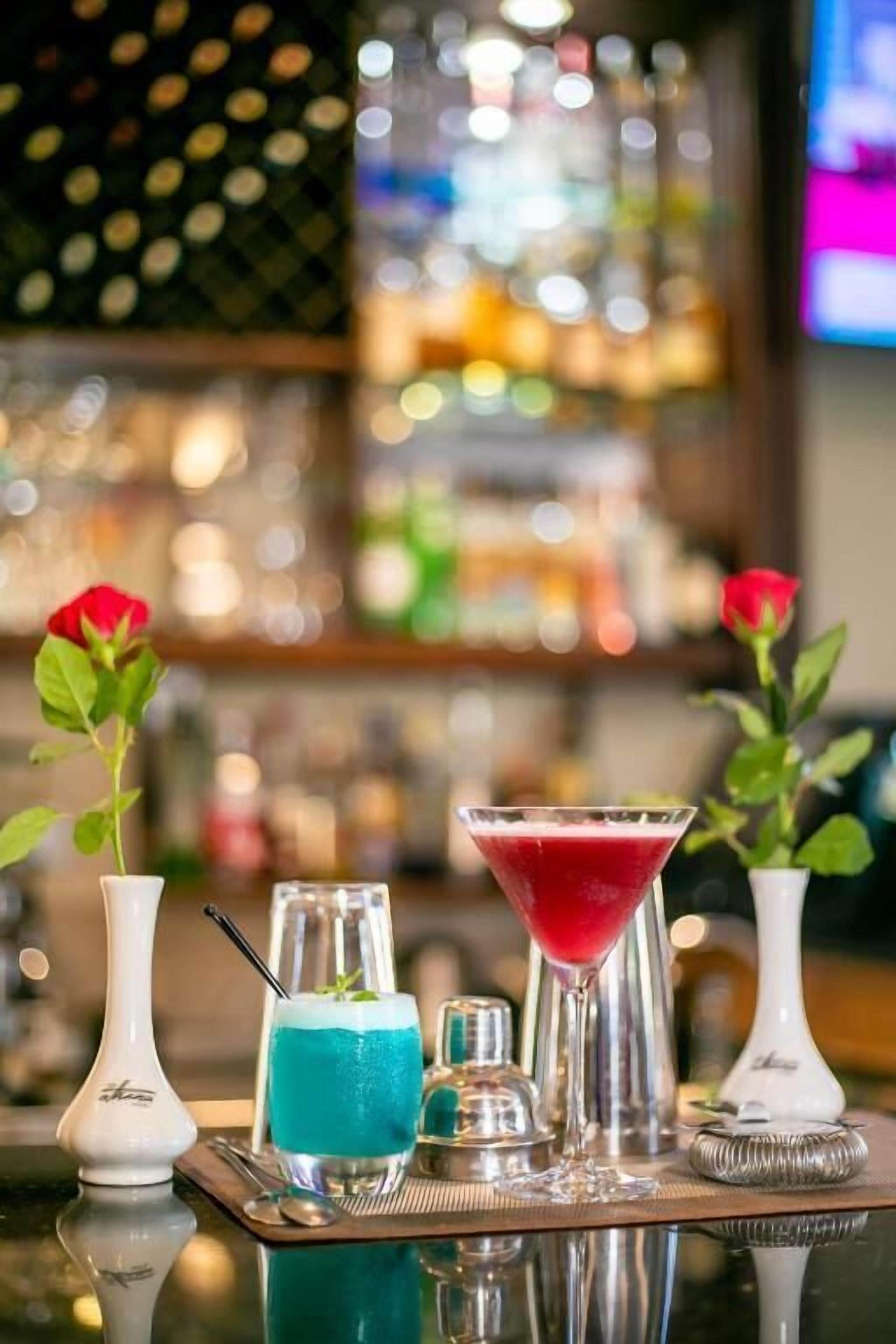 Un bar con una bandeja que sostiene una copa de martini, un cóctel azul y una rosa en un jarrón.