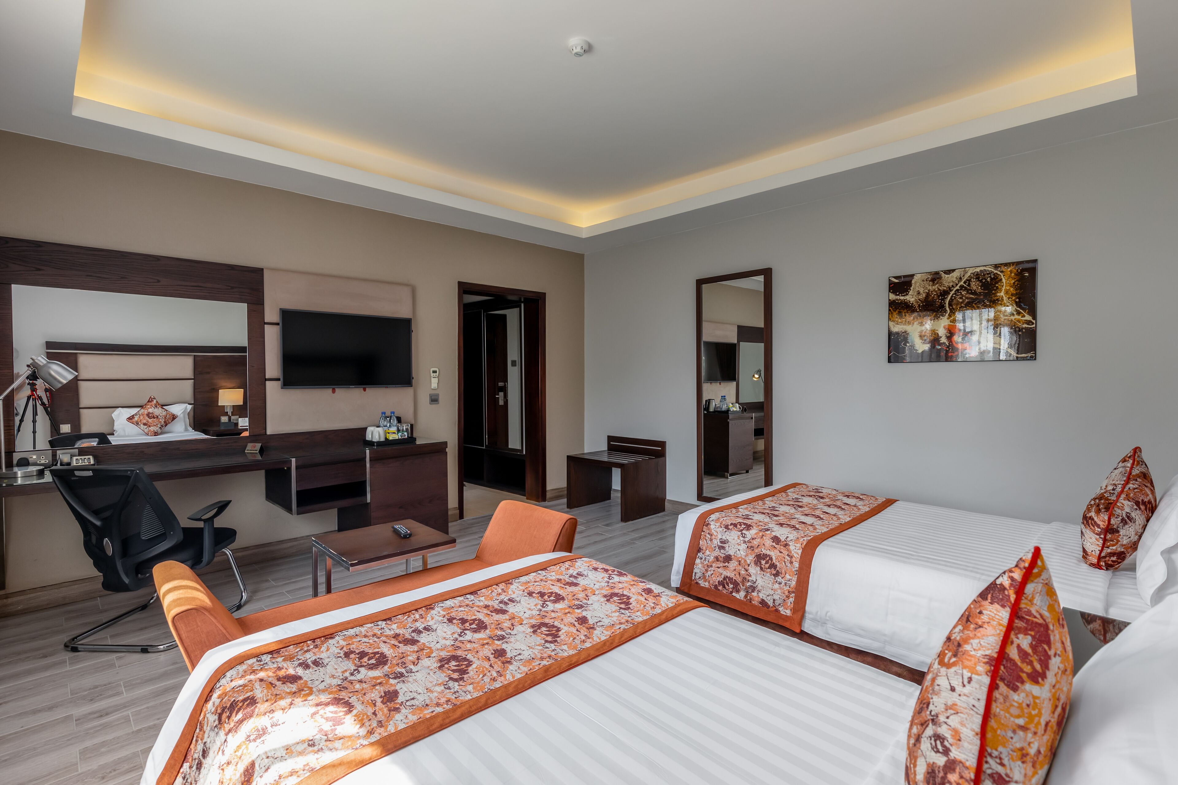 A hotel room with two beds, a desk, a chair, a TV, and a mirror.