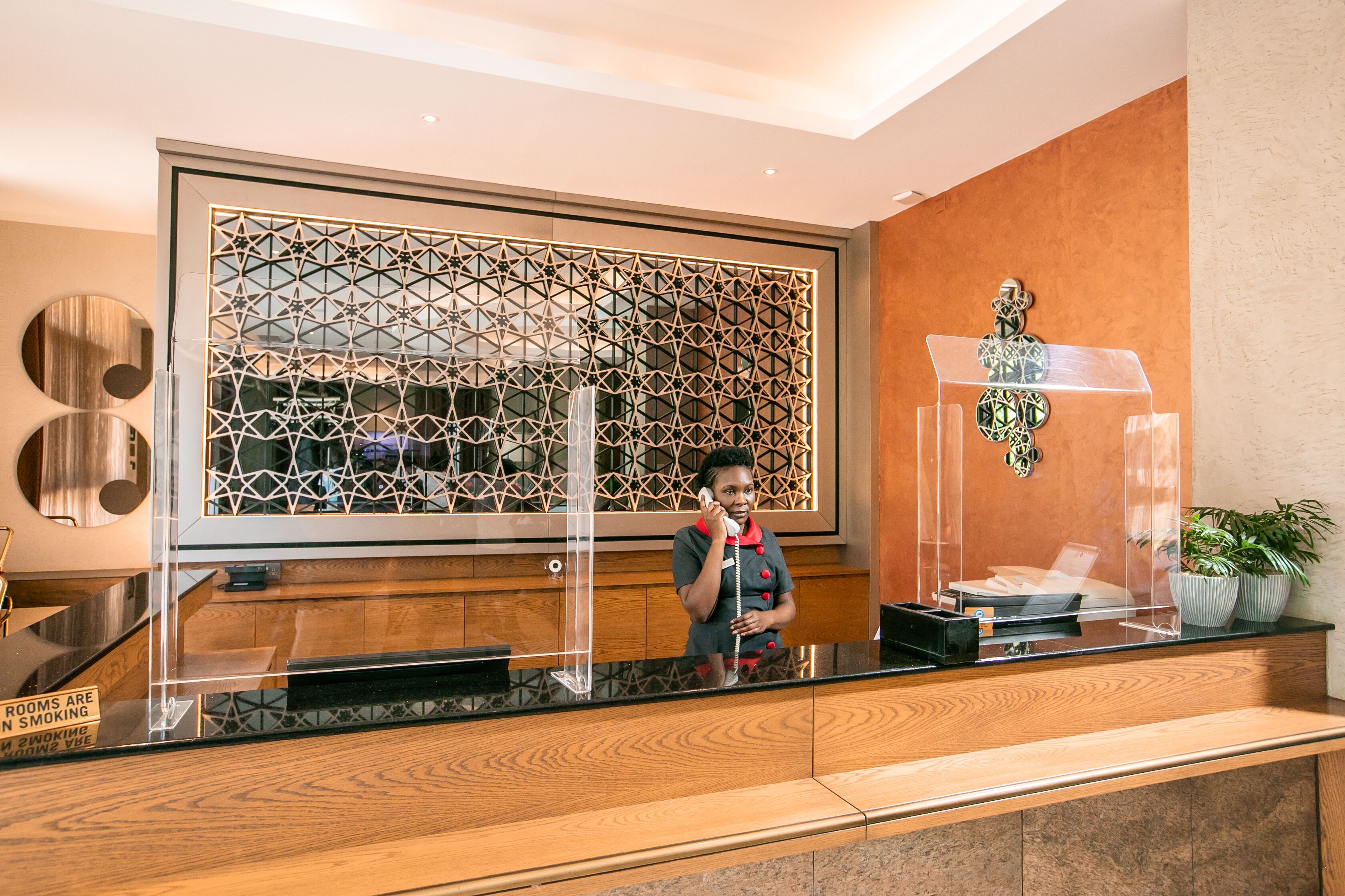 A reception desk with a geometric patterned backdrop, a clear glass partition, and a wooden counter.