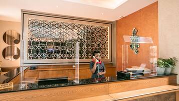 A reception desk with a geometric patterned backdrop, a clear glass partition, and a wooden counter.