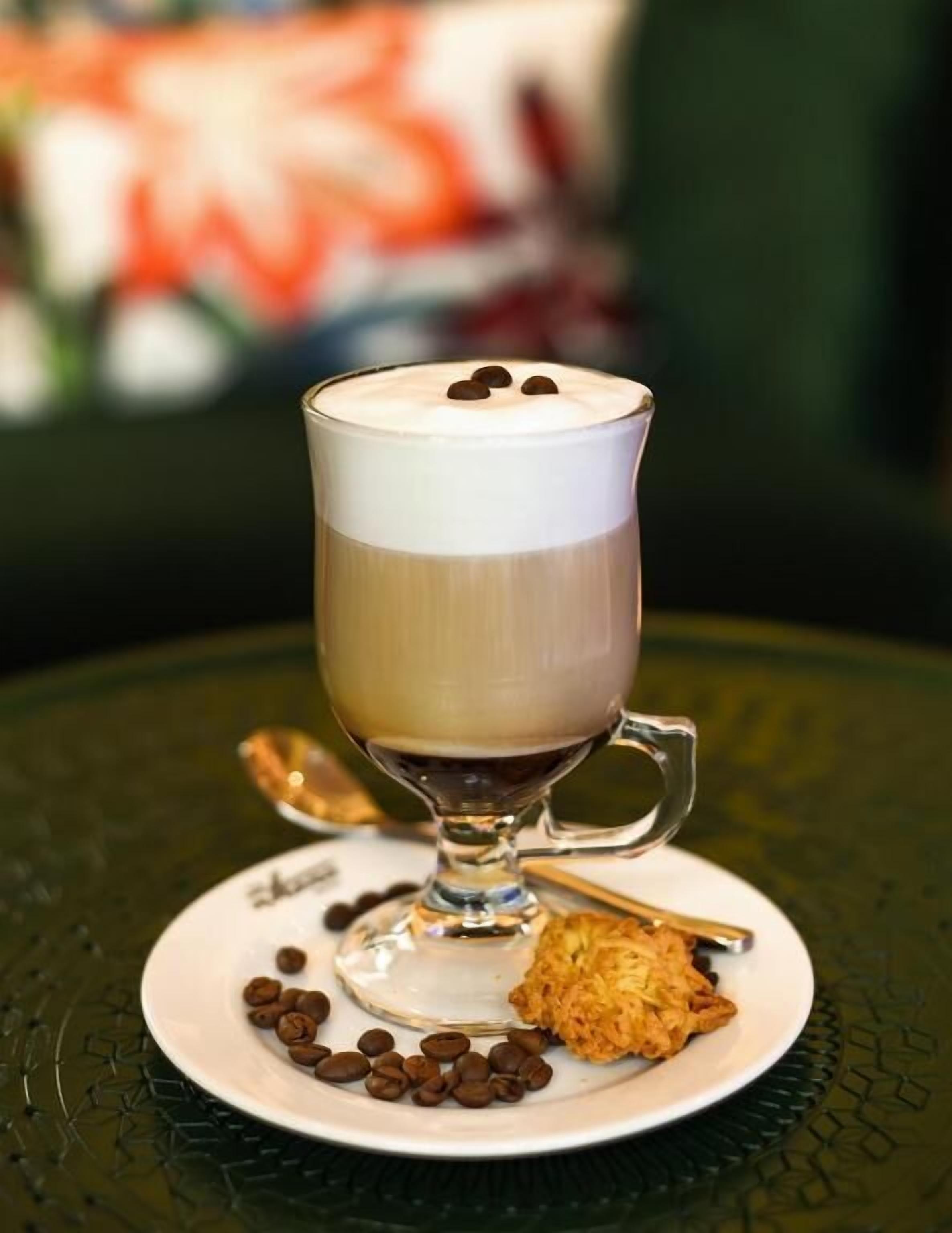 Una taza de café con crema batida y chispas de chocolate sobre un plato, junto con una cuchara y granos de café.