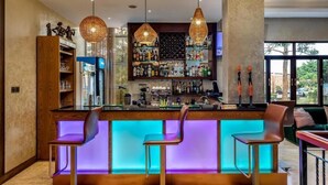 Un espace bar doté d'un comptoir illuminé par des néons, de trois tabourets de bar et d'un éclairage suspendu au plafond.