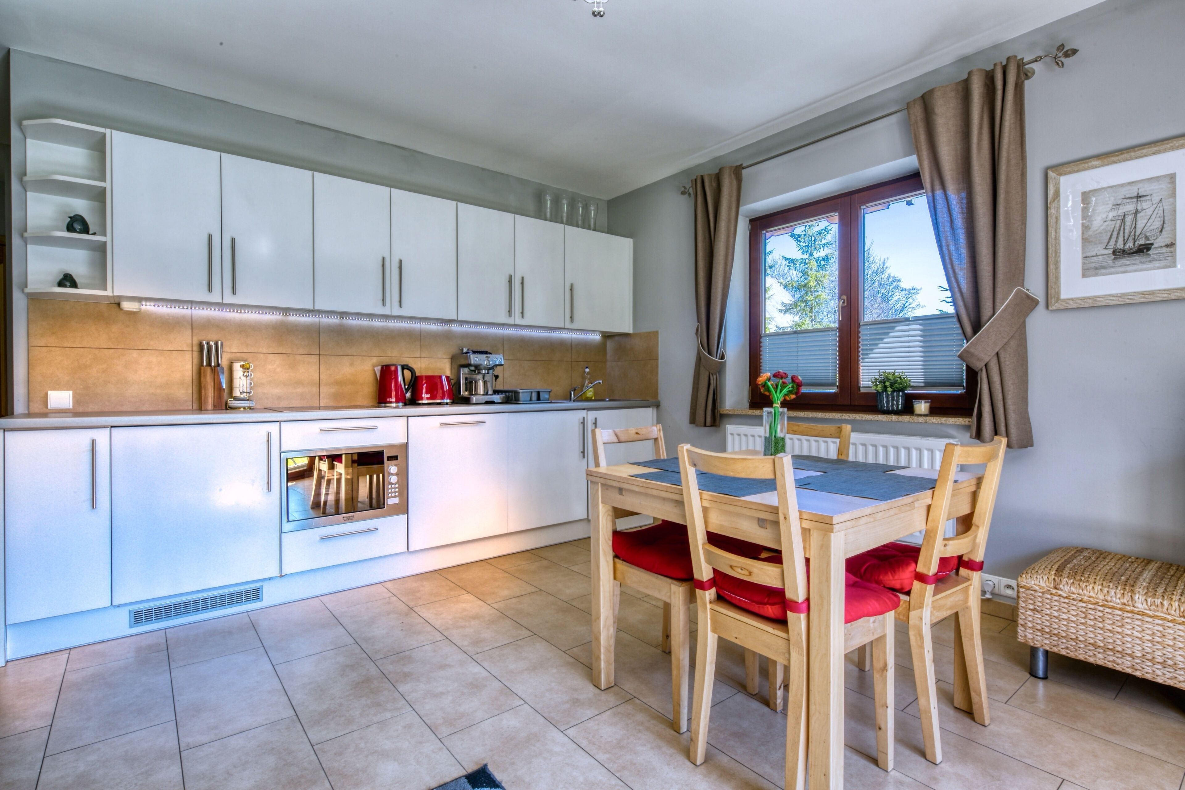 A modern kitchen with white cabinets, a dining table with chairs, and a window with curtains.