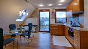 A modern kitchen with a glass dining table, wooden cabinets, and a view of the city through large windows. - Apartament Ogrody Górskie widok na Tatry (Zakopane)