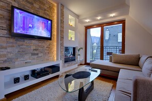 A modern living room with a flat-screen TV mounted on a stone wall, a glass coffee table, a beige sofa, and a fireplace. - Apartament Ogrody Górskie widok na Tatry (Zakopane)