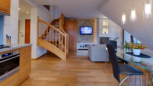 A modern kitchen with wooden cabinets and a built-in oven, a dining area with a glass table and chairs, and a living room with a TV and decorative lights. - Apartament Ogrody Górskie widok na Tatry (Zakopane)