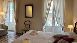 A hotel room with a bed, a chair, a desk, a lamp, and a window with curtains.