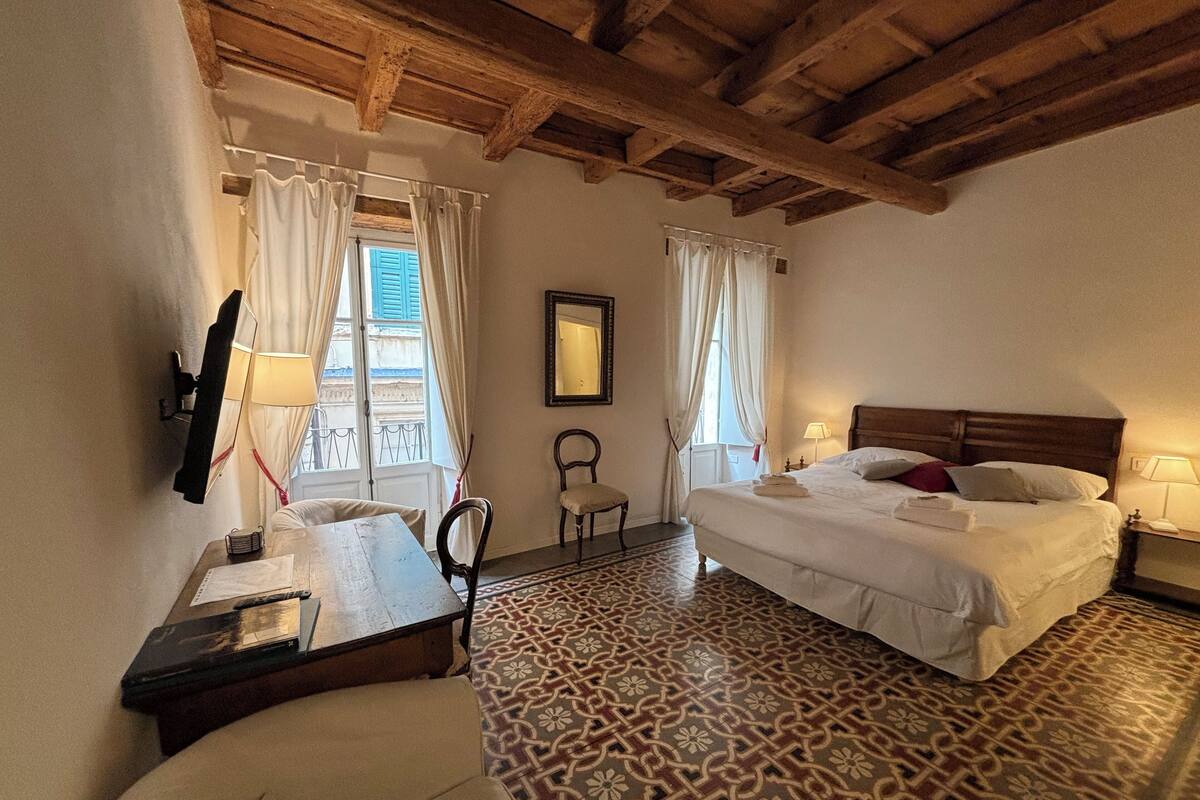 Ein Hotelzimmer mit zwei Betten, einer Holzbalkendecke, Fliesenboden mit Muster, einem Schreibtisch mit Stuhl und einem kleinen Tisch.