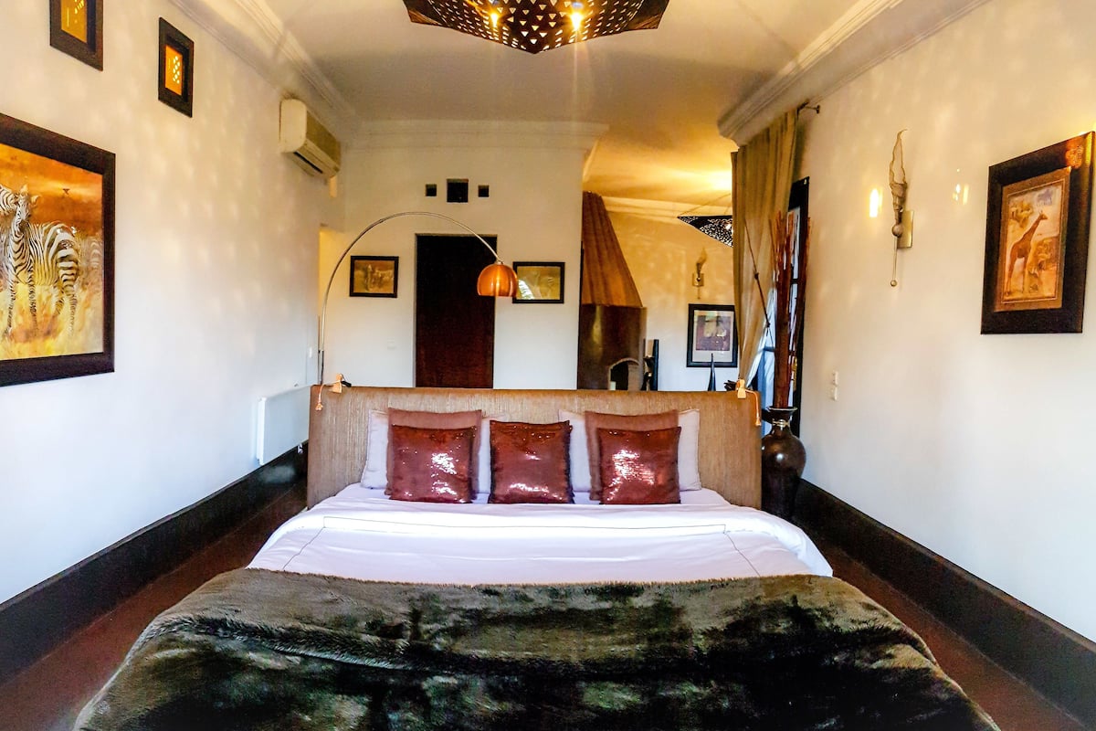 A hotel room with a large bed, a headboard, a mirror, and framed artwork on the walls.