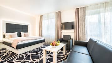 Hotellihuone, jossa on sänky, sohva, televisio ja pöytä, jonka päällä on hedelmiä.