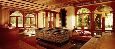 A spa area with a large hot tub, wooden benches, and large arched windows.