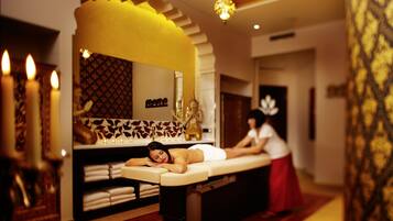 Ett spa-rum med en massagebänk, ljus och en person som får massage.
