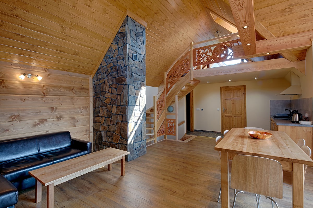 A wooden interior with a stone accent wall, a wooden staircase, a dining area, and a kitchen.