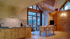 A kitchen with wooden cabinets, a large window, and a dining area with chairs and a table. - Tatrzańskie Echo Domki Regionalne (Zakopane)