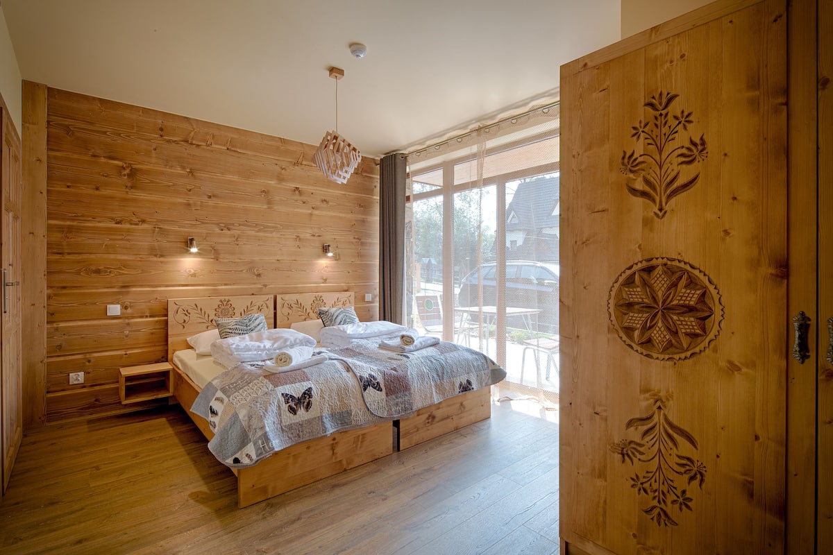 A wooden bedroom with a bed, built-in bench, and large windows.