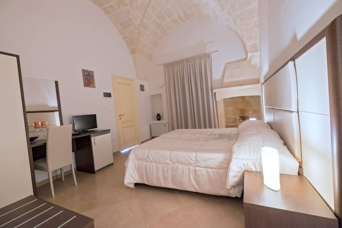 Quarto com cama, escrivaninha, cadeira e televisão.