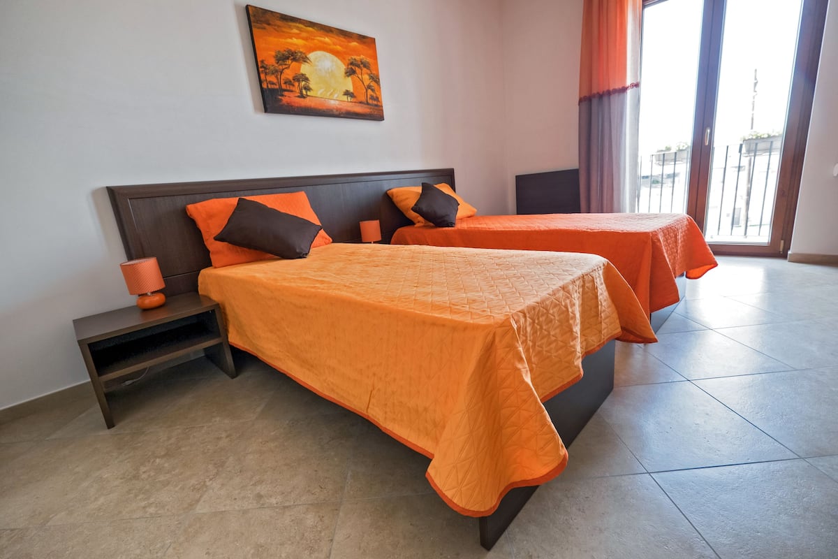 Quarto de hotel com duas camas, uma mesinha de cabeceira, um abajur e um quadro na parede.